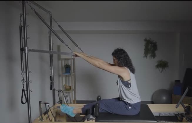 A one-to-one session at Axis Pilates: a client seated on the reformer pulling the Tower roll-down bar