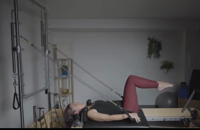 A client lying on the reformer under the Tower with the straps overhead